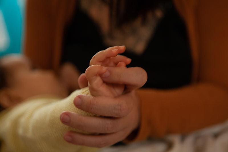 Mãe segurando a mão de bebê enquanto amamenta